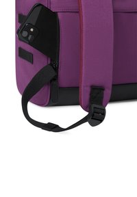 Lila Rucksack mit einer strukturierten Oberfläche, ausgestattet mit einer Seitentasche mit Reißverschluss, die ein schwarzes Smartphone enthält, sowie einem schwarzen Tragegurt mit Clip.