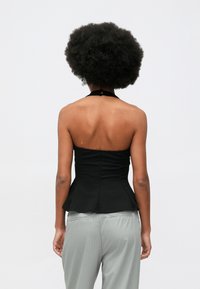 Čierny peplum top s dizajnom na halterneck, ktorý má priliehavý strih a hladkú textúru, spárovaný so svetlo šedými prúžkovanými nohavicami.