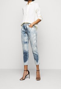 Světlé denimové džíny s vybledlým vzhledem, vysokým pasem a rovnými nohavicemi. Spárované s bílou košilí z lnu s knoflíky a černými podpatky.