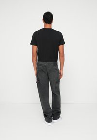 Camiseta negra combinada con pantalones cargo holgados de color gris oscuro con múltiples bolsillos y detalles en rojo. Se lleva con zapatillas blancas.