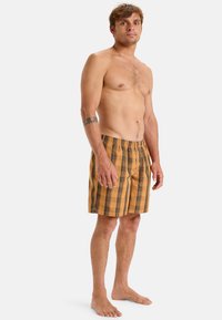 Bañador masculino en un patrón de cuadros en amarillo y negro, tejido ligero, cinturilla elástica, de largo hasta la rodilla, transpirable y con un diseño casual.
