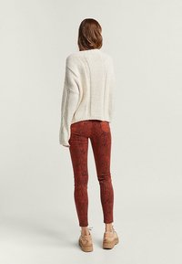 Overdsize crèmekleurige gebreide trui met ribbelstructuur, gecombineerd met strakke rode slangenprint broek en beige chunky platform schoenen.