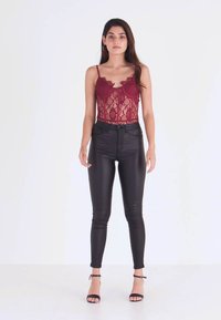 Burgundy lace bodysuit with floral pattern, paired with black fitted leather pants. Model wears black heeled sandals, standing against a white background.