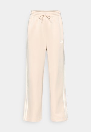 Béžové tepláky s volným střihem, elastickým pasem, šňůrkou na stažení a bílými pruhy po stranách. Na levé stehně je logo Adidas.