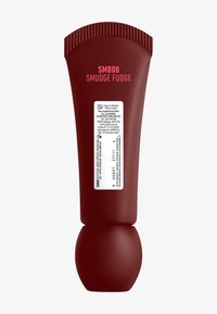 Tube souple rouge avec un capuchon strié, étiqueté "SMB08 SMUDGE FUDGE." Présente une base arrondie et les détails des ingrédients au dos.
