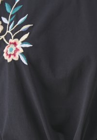 Zwarte stoffen top met kleurrijke bloemenborduursels in tinten rood, blauw en crème, met groene bladeren. Gladde textuur, close-up weergave.