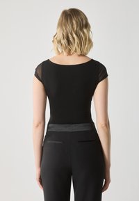 Top negru ajustat cu mâneci scurte transparente, guler rotund. Asortat cu pantaloni negri cu talie înaltă, care au un brâu din satin și buzunare la spate.