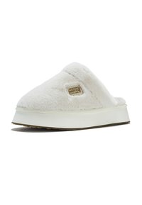 Chausson blanc duveteux avec un dessus en peluche, une semelle épaisse blanche et une semelle extérieure en caoutchouc texturé ; présente une petite étiquette rectangulaire avec logo.