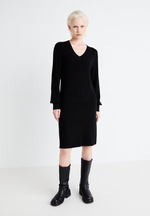 Black knit dress with a V-neckline and long sleeves, featuring a straight cut and textured fabric. Paired with knee-high black boots.