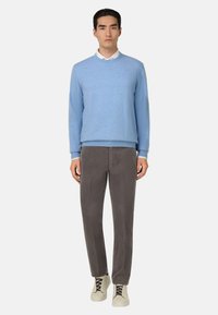 Suéter azul claro con cuello redondo, combinado con pantalones de pana grises y zapatillas crema. Diseño simple y limpio con acentos mínimos.