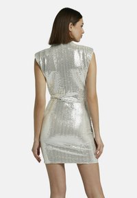 Robe courte en métal argenté avec des manches courtes et une silhouette ajustée. Confectionnée en tissu pailleté, elle présente un détail de taille cintrée.
