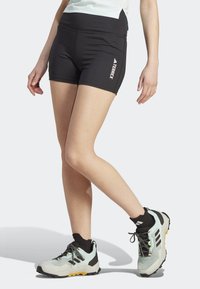 Černé sportovní kraťasy s vysokým pasem a bočními kapsami, s bílým logem "TERREX". Nosené s světlými trailovými botami.