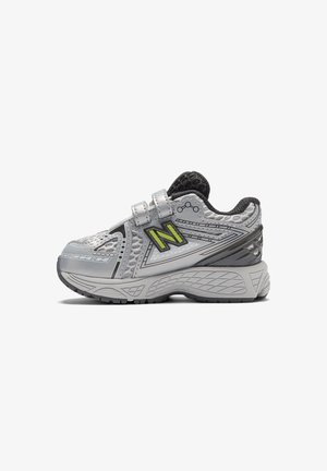 Gray athletic shoe with a textured upper, mesh accents, yellow "N" logo, and Velcro strap. Features a cushioned sole with tread.