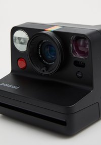 Black Polaroid camera with a round lens, red shutter button, dual flash, and a colorful stripe across the top. Engraved logo on the front.