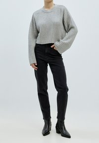 Grauer gerippter, knapper Pullover mit weiten Ärmeln, kombiniert mit hochgeschnittenen schwarzen Jeans und schwarzen Absatzstiefeln. Einfaches und modernes Design.