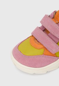 Baskets colorées avec du daim rose, du cuir vert et des accents orange. Trois brides à Velcro et une semelle en caoutchouc arrondie avec des coutures discrètes.