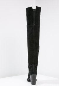 Bottes noires en daim au-dessus du genou avec des fentes latérales, un talon haut et des coutures visibles sur la couture arrière, mettant en avant une texture lisse.