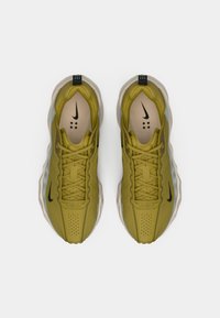 Oliwkowe buty sportowe z gładką cholewką, perforowanymi detalami, jasnobrązową wkładką i czarnymi akcentami z logo po bokach oraz na pięcie.