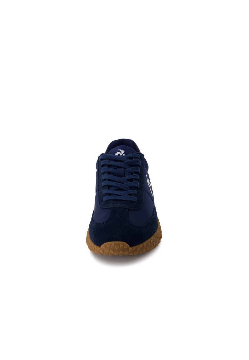 Zapatilla azul marino con materiales de ante y sintéticos, suela de goma, diseño con cordones y un acento de logo en el lado. Lengüeta plana con acolchado.