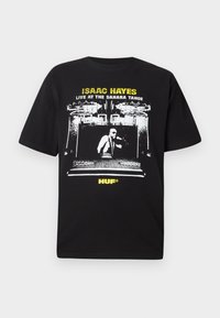Sort bomulds t-shirt med et grafisk tryk af en musiker i en scene, med hvid og gul tekst: "ISAAC HAYES LIVE AT THE SAHARA TAHOE."