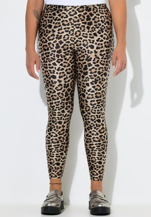 Person iført leopardmønstrede leggings med højtaljede og metalliske platform loafers, stående mod en ensfarvet hvid baggrund.