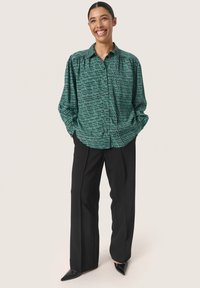 Groene gestreepte blouse met een losse pasvorm, lange mouwen en een klassieke kraag, gecombineerd met strakke zwarte broek en puntige schoenen.