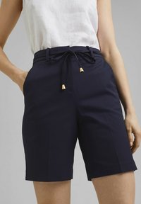 Pantalones cortos azul marino con un diseño a medida, que cuentan con una cintura ajustable con cordón, detalles en dorado en las puntas del cordón y bolsillos laterales.