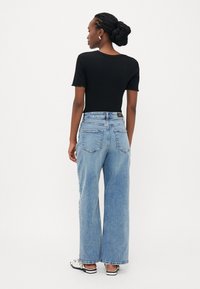 Μαύρο ριχτό κοντομάνικο τοπ συνδυασμένο με ψηλόμεσα ανοιχτό μπλε φαρδιά παντελόνια. Τα παντελόνια διαθέτουν κλασικό σχέδιο με πέντε τσέπες.