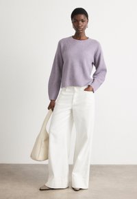 Lavendel strikket genser med ribbet tekstur og senkede skuldre, kombinert med høyt liv hvite vide bukser og en beige skulderveske.