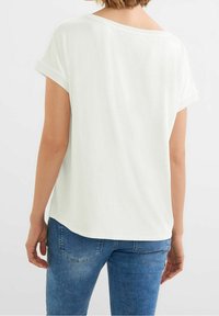 Vit t-shirt med kort ärm och avslappnad passform, med en vid halsringning och subtila ribbdetaljer, ihop med blå jeans.