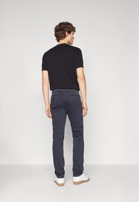 Pantaloni navy in cotone con vestibilità slim, dotati di tasche posteriori e dettaglio con cerniera, abbinati a sneaker bianche e una t-shirt nera.
