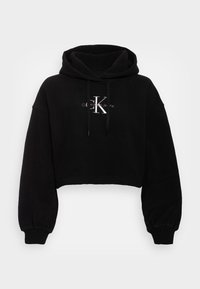 Felpa corta nera realizzata in tessuto morbido, con un ampio cappuccio, maniche lunghe e un logo frontale in filo argentato. Polsini e orlo a coste.