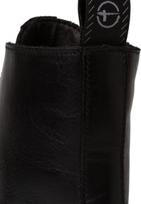 Bottine en cuir noir avec texture lisse, sommet arrondi, coutures contrastées et une languette en tissu avec un logo en relief.