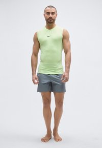Fitted light green sleeveless athletic top with black Nike logo, paired with grey shorts. Model is barefoot against a plain background.