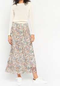 Długa, zwiewna spódnica z lekkiego materiału, zdobiona wielokolorowym wzorem paisley. Połączona z kremową bluzką z długim rękawem i białymi sneakersami.