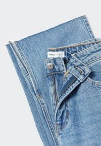 Jean en denim bleu clair avec une braguette zippée, une fermeture à bouton en métal et des coutures visibles. L'étiquette affiche des informations sur la marque et la taille.