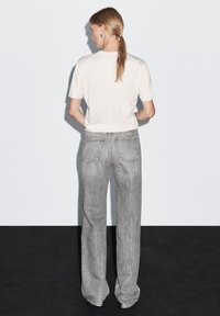 White short-sleeve t-shirt paired with high-waisted gray denim jeans. The jeans have back pockets and a straight-leg design, featuring subtle fading.