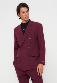 Blazer bordeaux doppiopetto realizzato in tessuto liscio, con bottoni neri, colletto a pieghe e tasche laterali per una vestibilità strutturata.