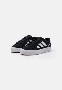 Black suede sneakers with white stripes, flat white rubber sole, and black laces. Features a low-top design and padded collar.