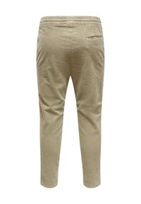 Pantalones de pana beige con una superficie texturizada, cinturilla elástica y un único bolsillo trasero. Piernas ajustadas con un acabado suave en los puños.