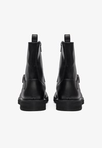 Botas de cuero negro hasta el tobillo con una textura suave, que cuentan con una cremallera trasera y una suela robusta para durabilidad y tracción.