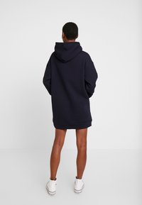 Vestido sudadera de gran tamaño en color marino con una capucha grande, puños y dobladillo acanalados. Combinado con zapatillas blancas, muestra un ajuste relajado y una textura suave.