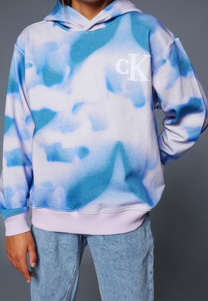 Hoodie violet clair avec un motif abstrait bleu et blanc, comportant une poche kangourou à l'avant et un petit logo "cK" blanc. Matière douce.