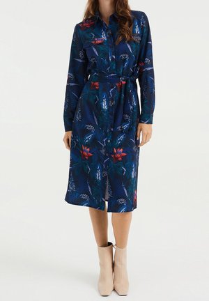 Niebieska sukienka koszulowa w kwiaty z zapięciem na guziki z przodu, z paskiem w talii i do kolan. Materiał ma gładką fakturę i żywy nadruk.
