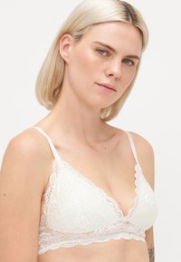 Witte kanten bralette met geschulpte randen, doorzichtige stof en dunne verstelbare bandjes. Bloemenpatroon door het hele ontwerp, wat zorgt voor een delicate uitstraling.