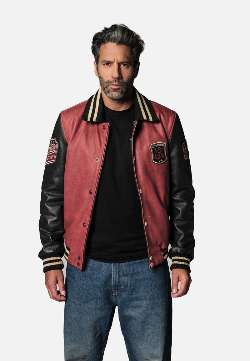 Veste varsity en cuir rouge et noir avec col et poignets en coton rayé, dotée de patches et d'une fermeture à bouton pression. Portée sur une chemise noire.