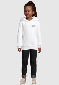 White hoodie with front pocket, featuring "Dreams Over Reality" text in teal. Paired with dark leggings and light shoes with fluffy accents.