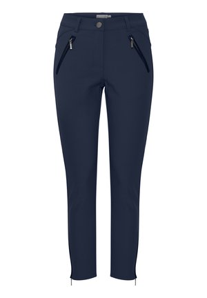 Tamsiai mėlynos kelnės su siauru kirpimu, šoninėmis užtrauktukais uždaromomis kišenėmis, priekiniais mygtukais uždarančia sistema ir užtrauktukais ties kulkšnimis, leidžiančiais reguliuoti ilgį.