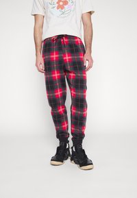 Rode en zwarte geruite joggers met elastische cuffs en een verstelbare tailleband, gemaakt van zachte stof. Gecombineerd met zwarte sneakers.
