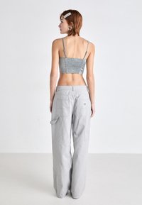 Top corto plateado con la parte trasera fruncida, combinado con pantalones cargo de pierna ancha en gris claro que cuentan con dos bolsillos traseros y sutilezas en los detalles de costura.